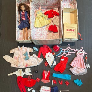 Puede incluir: Una muñeca Skipper vintage con un guardarropa de ropa y accesorios. La muñeca está en una maleta con un interior floral. La ropa incluye vestidos, abrigos, zapatos y un sombrero rojo. También hay una caja de accesorios Skipper.
