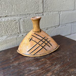 Może przedstawiać: Mały, trójkątny wazon ceramiczny z wąskim szyjką i geometrycznym wzorem w czarnej glazurze. Wazon jest jasnobrązowy z fakturowaną powierzchnią.