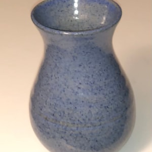 Könnte beinhalten: Eine kleine, hellblaue Keramikvase mit einem gesprenkelten Überzug. Die Vase hat einen runden Körper und eine schmale Öffnung.