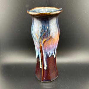 Puede incluir: Un jarrón de cerámica alto y delgado con un esmalte marrón oscuro y un esmalte blanco y azul que gotea por los lados. El jarrón tiene una abertura ligeramente acampanada y un fondo redondeado.