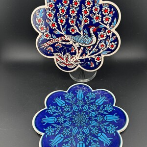 May include: Two ceramic decorative plates with a floral design. The top plate features a blue background with a bird and floral pattern in red, white, and blue. The bottom plate has a blue floral pattern on a blue background.