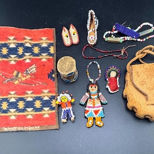 May include: A collection of Native American crafts, including a small rug with a geometric design and a figure with a bow and arrow, beaded dolls, moccasins, a small drum, and a leather pouch.