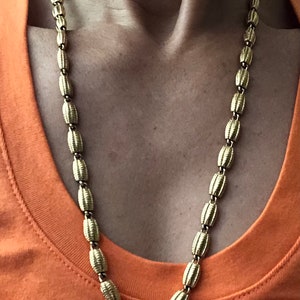 May include: A gold chain necklace with oval-shaped links. The chain is worn by a person, but the person's face is not visible.