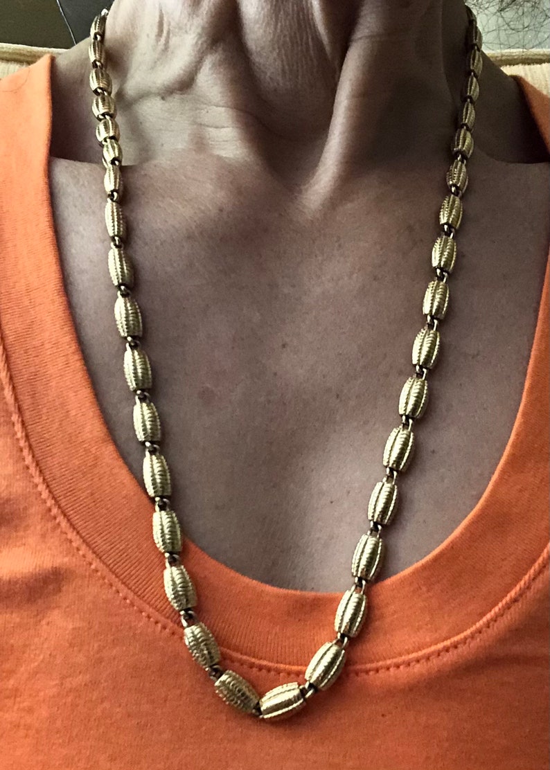 May include: A gold chain necklace with oval-shaped links. The chain is worn by a person, but the person's face is not visible.