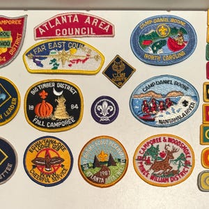 Może przedstawiać: Kolekcja kolorowych haftowanych naszywek z różnymi nazwami oddziałów harcerskich, lokalizacjami i datami. Naszywki mają kształt okrągły, prostokątny i owalny z różnymi wzorami, w tym dynią, ogniskiem, rzeką i emblematem harcerskim.