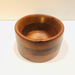 May include: A small, round wooden bowl with a dark brown stain. The bowl has a natural wood grain pattern and is made of multiple pieces of wood.