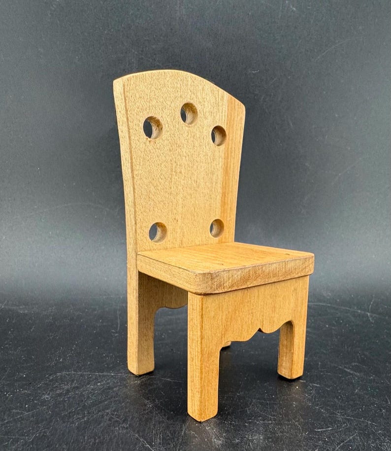 May include: A small, wooden chair with a light brown finish. The chair has a rectangular seat and a back with four circular cutouts. The legs are straight, and the back has a curved top. The chair is approximately 6 inches tall.