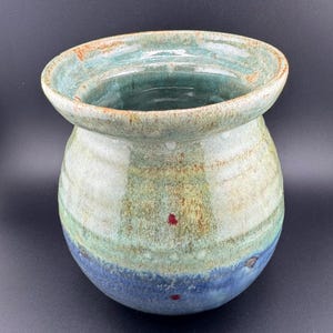 May include: A ceramic vase with a wide mouth and a rounded body. The vase is glazed in shades of green, blue, and brown with red speckles.