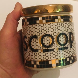 May include: A white ceramic jar with a gold lid and black and gold geometric design. The jar has the word "SCOOP" written in black letters on the front.