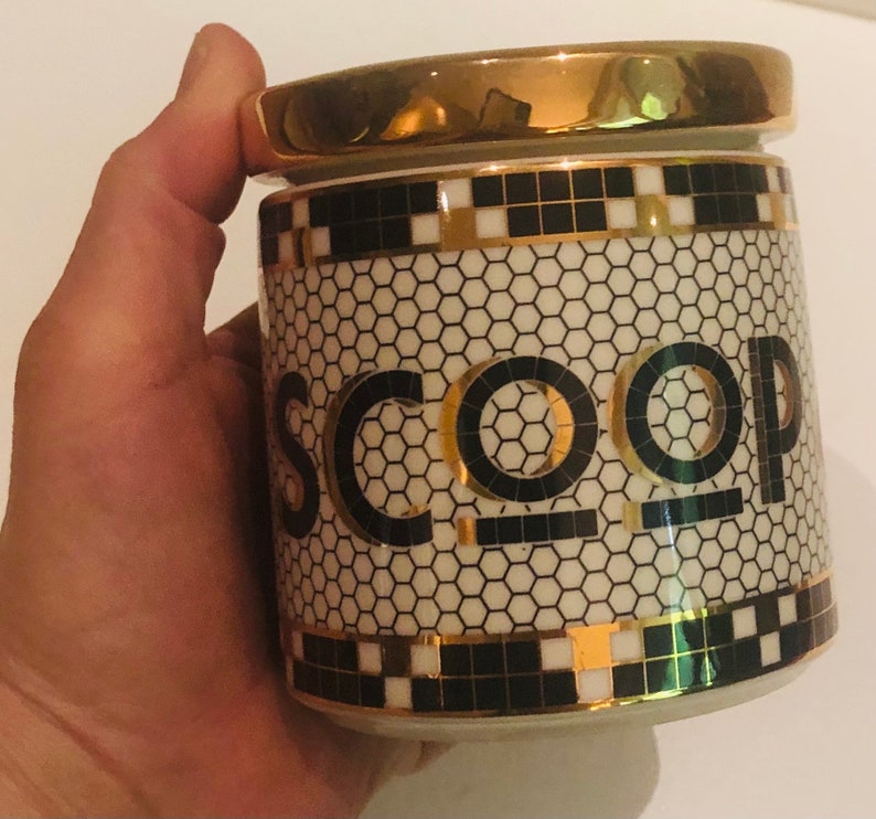 May include: A white ceramic jar with a gold lid and black and gold geometric design. The jar has the word "SCOOP" written in black letters on the front.