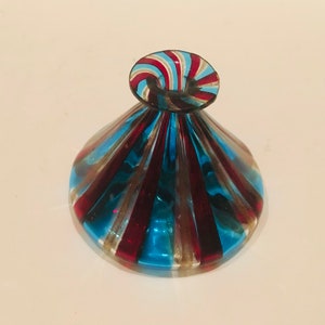 May include: A decorative glass ornament with a round base and a spiraled top. The glass is striped with red, blue, and gold colours. The piece has a unique shape and design.