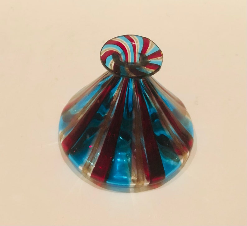 May include: A decorative glass ornament with a round base and a spiraled top. The glass is striped with red, blue, and gold colours. The piece has a unique shape and design.