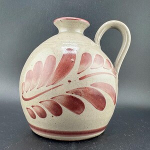 Peut inclure: Pichet en céramique beige avec un corps arrondi et une anse. Le pichet est décoré d'un motif de feuilles rouges et d'un bord rouge. Le pichet mesure environ 20 cm de haut.