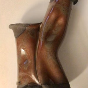 Puede incluir: Un jarrón de cerámica marrón con una forma abstracta única. El jarrón tiene un acabado brillante y una superficie texturizada.