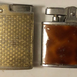 May include: Two vintage lighters, one with a gold-toned, textured finish and the other with a brown, marbled finish.