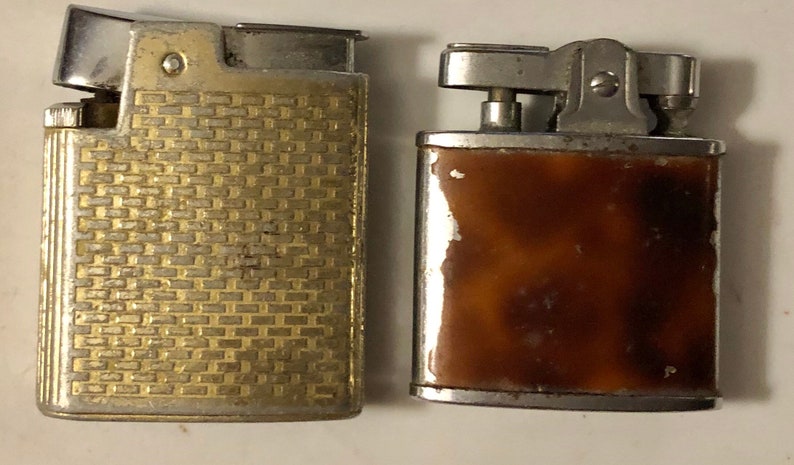 May include: Two vintage lighters, one with a gold-toned, textured finish and the other with a brown, marbled finish.