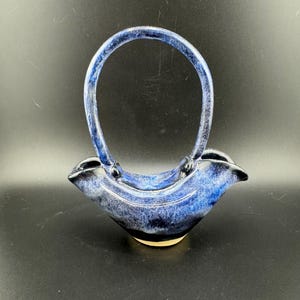 May include: A blue and black ceramic vase with a handle. The vase has a unique shape and is perfect for displaying flowers.