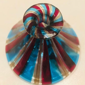 May include: A decorative glass object with a flared base and a rounded top. The design features alternating stripes of blue, red, and gold. The object appears to be a small vase or a unique drinking glass.