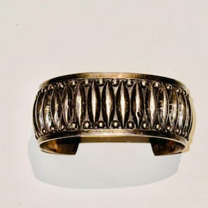 Puede incluir: Un brazalete de plata con un patrón repetitivo de formas ovaladas y pequeñas cuentas.