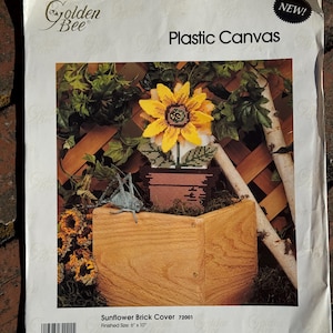 May include: A craft kit for a sunflower brick cover. The image on the package shows a stitched sunflower in a wooden planter. The finished size is 6" x 10". The kit includes plastic canvas, yarn, graph, needle, and instructions.
