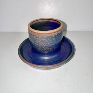 May include: A blue and brown ceramic cup and saucer set. The cup has a speckled glaze and a brown rim. The saucer is a solid blue with a brown rim.