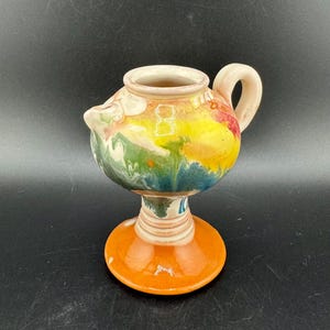 Peut inclure: Un pichet en céramique coloré avec un motif en spirale dans des tons de vert, bleu, jaune, orange et blanc. Le pichet a une poignée et une base large.