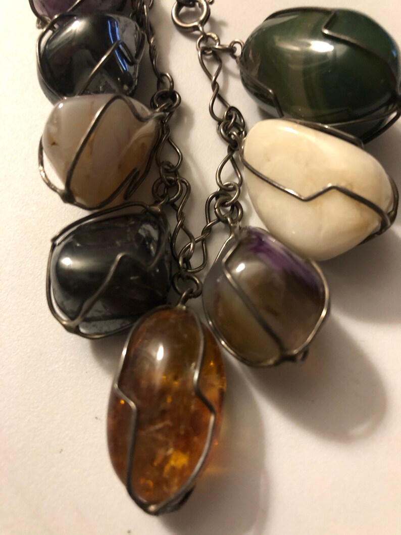 Pode incluir: Um bracelete de corrente de prata com uma variedade de contas de pedras preciosas, incluindo ametista, &aacute;gata, &acirc;mbar e hematita. Cada conta &eacute; envolvida em fio de prata.