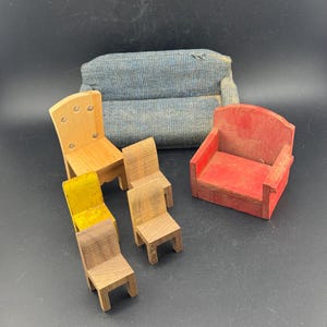 May include: A collection of miniature wooden furniture, including a blue upholstered sofa, a red armchair, and several small chairs in various wood tones. One chair has a yellow seat. The furniture is arranged on a dark surface.