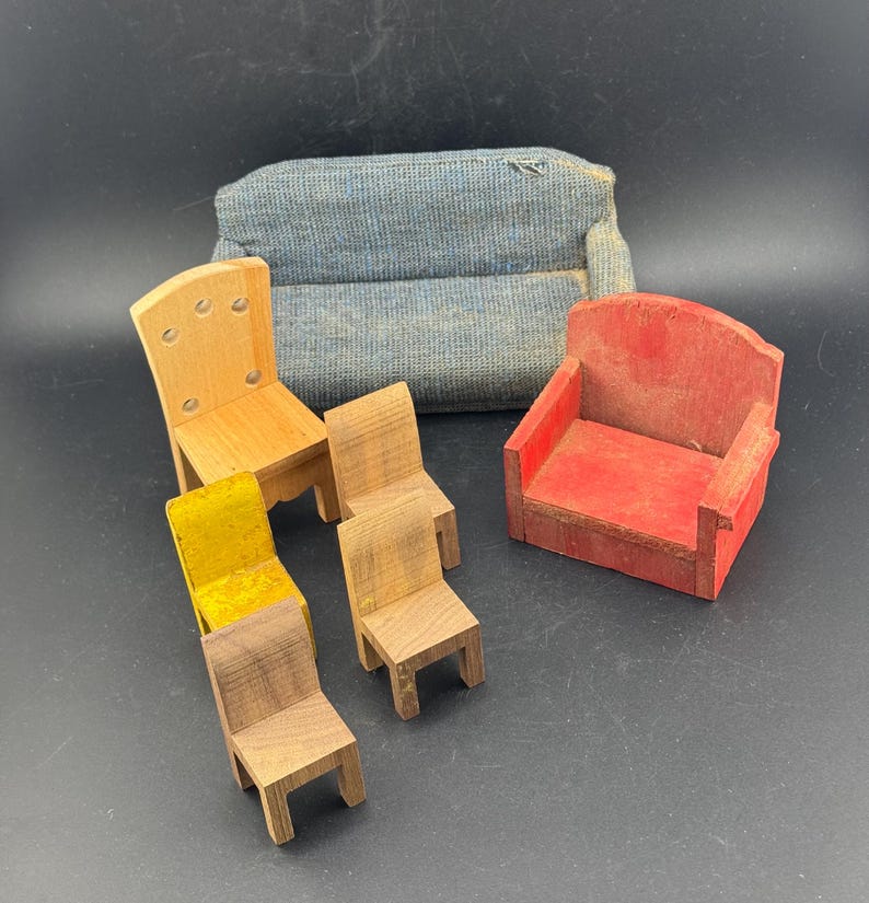 May include: A collection of miniature wooden furniture, including a blue upholstered sofa, a red armchair, and several small chairs in various wood tones. One chair has a yellow seat. The furniture is arranged on a dark surface.