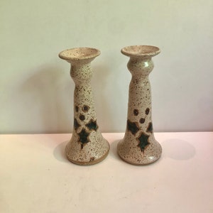 May include: A pair of white ceramic candle holders with a speckled finish and green and brown holly leaf designs.