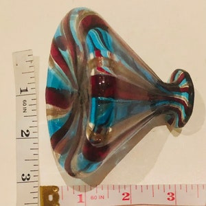 May include: A decorative glass vase with a flared opening and a bulbous body. The vase features a swirl design in shades of blue, red, and gold. The vase is approximately 7.6 cm in height.