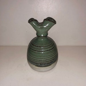 Pode incluir: Um vaso de cerâmica verde com um bico único em forma de pássaro. O vaso tem um design texturizado em listras e uma base branca.