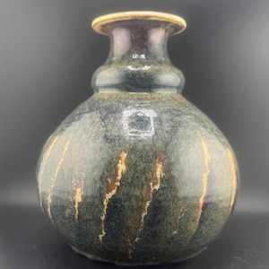 以下が含まれることがあります： 丸みを帯びたボディと細い首を持つ、手作りのセラミック花瓶。 花瓶は、金と茶色の垂直ストリークを備えた濃い緑と青の釉薬が特徴です。 リムは薄いタン色です。