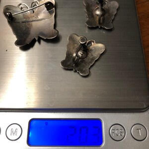 May include: Three silver butterfly brooches, two with earring backs and one with a pin back. The brooches are on a digital scale that reads 20.3 grams.