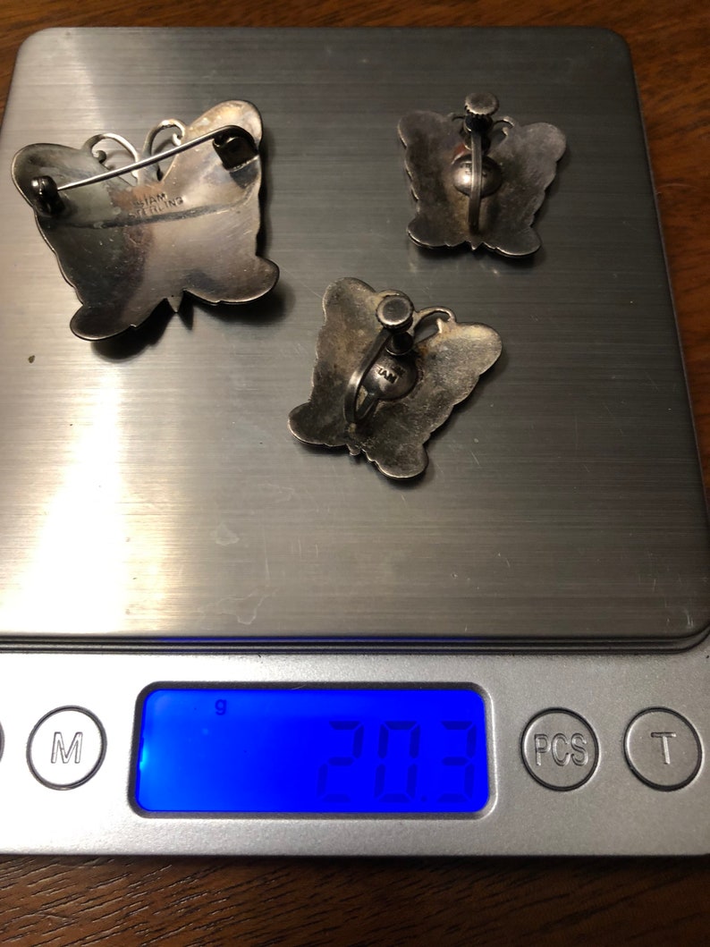 May include: Three silver butterfly brooches, two with earring backs and one with a pin back. The brooches are on a digital scale that reads 20.3 grams.