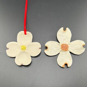 May include: Two white ceramic dogwood flower ornaments. One ornament has a yellow center and the other has an orange center.