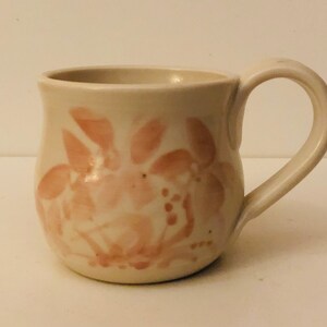May include: A white ceramic mug with a pink floral design. The mug has a rounded body and a handle.