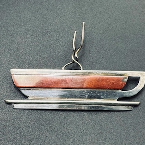 Pode incluir: Um broche de prata em forma de chávena e pires, com uma incrustação horizontal de pedra castanho-avermelhada no centro da chávena. A peça inclui uma fina argola de fio de prata torcido no topo para fixação, com um acabamento polido.