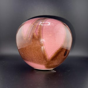 Könnte beinhalten: Eine runde Keramikvase mit einer rosa und braunen Glasur. Die Glasur hat ein wirbelndes Muster.