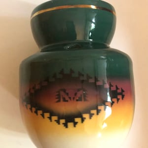 May include: A green ceramic vase with a gold rim and a Southwestern-style design. The vase has a white base with a yellow and brown gradient, and a black geometric pattern.