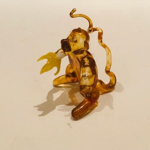 May include: A small, amber-colored glass monkey figurine with a curled tail and a yellow glass banana in its hand.