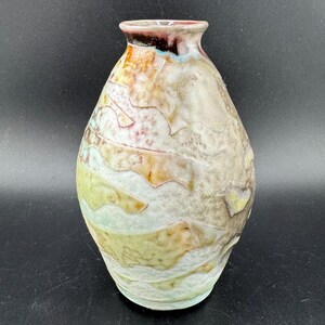 Könnte beinhalten: Eine Keramikvase mit rundem Körper und schmalem Hals. Die Vase hat eine strukturierte Oberfläche mit einer mehrfarbigen Glasur in Braun-, Gelb-, Grün- und Weißtönen.