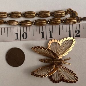 May include: A gold-tone chain necklace with a delicate butterfly pendant. The butterfly is made of thin wire and has a detailed design. The chain is made of linked oval-shaped pieces.