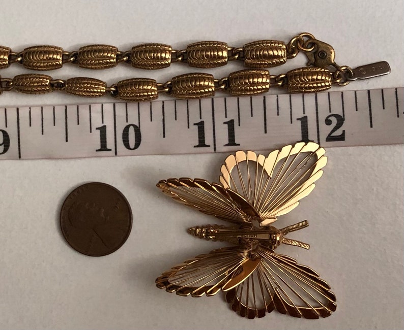 May include: A gold-tone chain necklace with a delicate butterfly pendant. The butterfly is made of thin wire and has a detailed design. The chain is made of linked oval-shaped pieces.