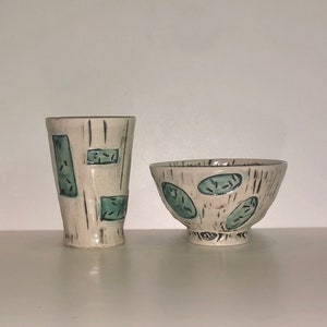 Peut inclure: Un ensemble de deux bols en céramique avec un fond blanc et des motifs géométriques verts et noirs. Le plus grand bol est plus large et moins profond que le plus petit.