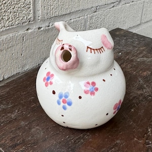 Puede incluir: Jarra de cerámica blanca con forma de cerdo con detalles en rosa y diseños florales azules y rosas.