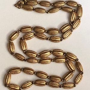 May include: A gold-toned chain necklace with a textured, oval-shaped link design. The necklace is made of metal and has a simple, elegant style.