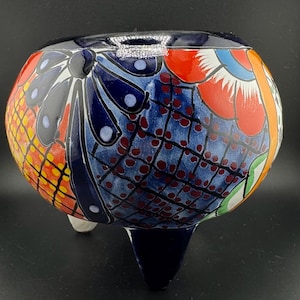 May include: A three-legged ceramic pot with a blue, red, white and yellow floral design. The pot is hand-painted with intricate details.