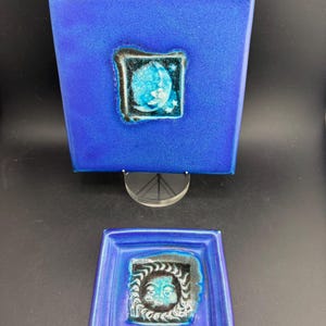 May include: Two-piece set of blue ceramic art pieces. The larger piece is square with a turquoise and black framed design. The smaller piece is rectangular with a similar design. Both pieces have a textured surface.
