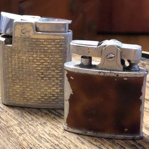 May include: Two vintage silver lighters. One lighter has a textured silver finish and the other has a brown plastic insert.